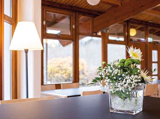 Tisch mit Blumenvase im Vordergrund und hölzerne Fenster durch die Licht eintritt
