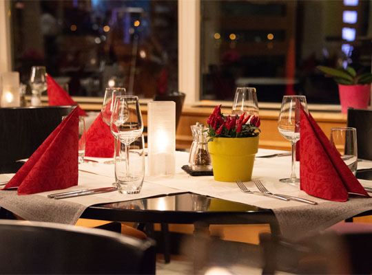 Festlich gedeckter Tisch mit roten Servietten und weißen Tischdecken, Kerzenschein im Hintergrund