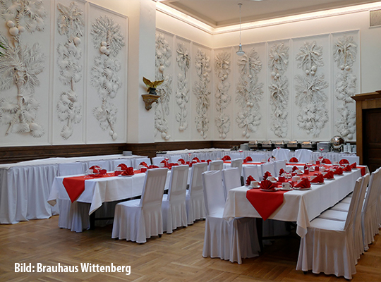 Großer Speisesaal mit antik gestalteter Wand, hoher Fensterdecke und liebevoll angerichteten Tischentafeln