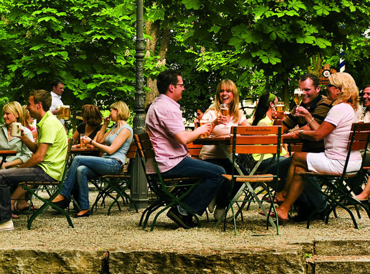 Biergarten des Hofbräukeller . Menschen sitzen beisammen und genießen das gute Wetter mit kalten Getränken und leckerem Essen 