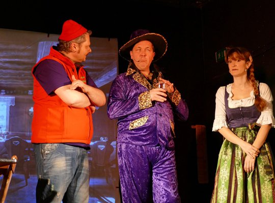 Ein Mann mit roter Mütze und Weste, einer in einem lila Samtanzug und eine Frau im Dirndl beim Krimidinner "Mord und Tod"